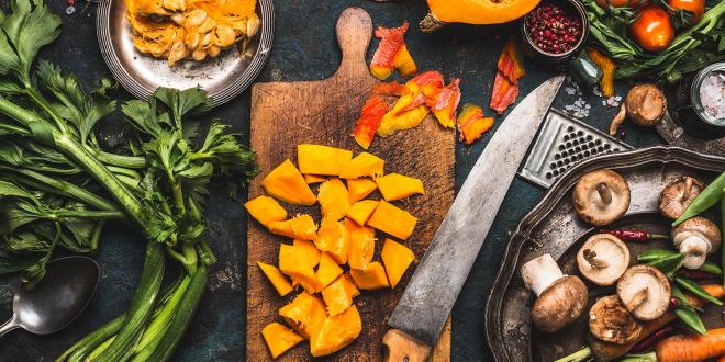 a kitchen knife on a cutting board of sliced and diced fruits and vegetables