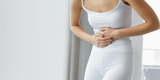 A woman in all white holding her stomach in pain.