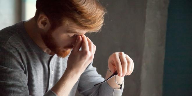 Tired red haired man massaging nose feeling fatigue from work.