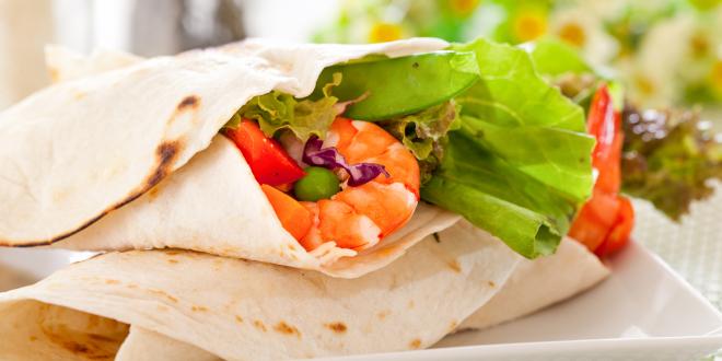 Prepared shrimp tacos on a white plate with flowers in the background.