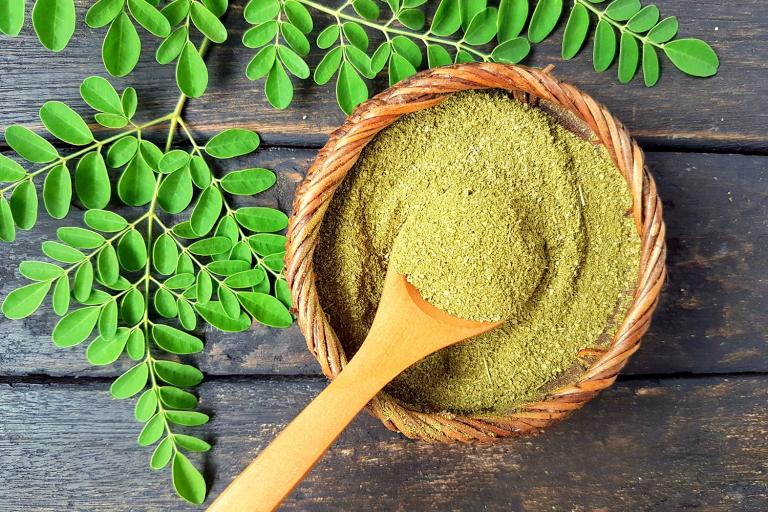 a bowl of moringa powder and fresh leaves