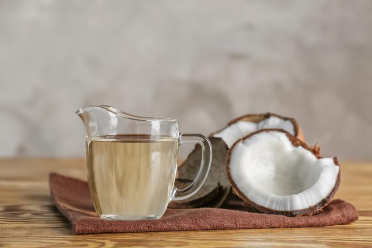 Ripe coconut and pitcher with MCT oil on a wooden table.