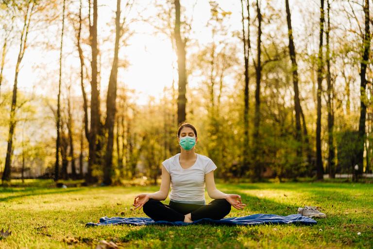 a woman wearing a mask, meditating in a sunny park