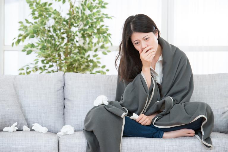 A woman on the couch with a blanket and a pile of tissues