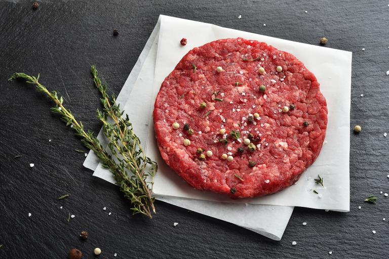 a seasoned burger patty ready to grill